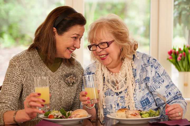 Two women smiling and chatting while sharing a delicious meal at the comfort of their spacious dining room.